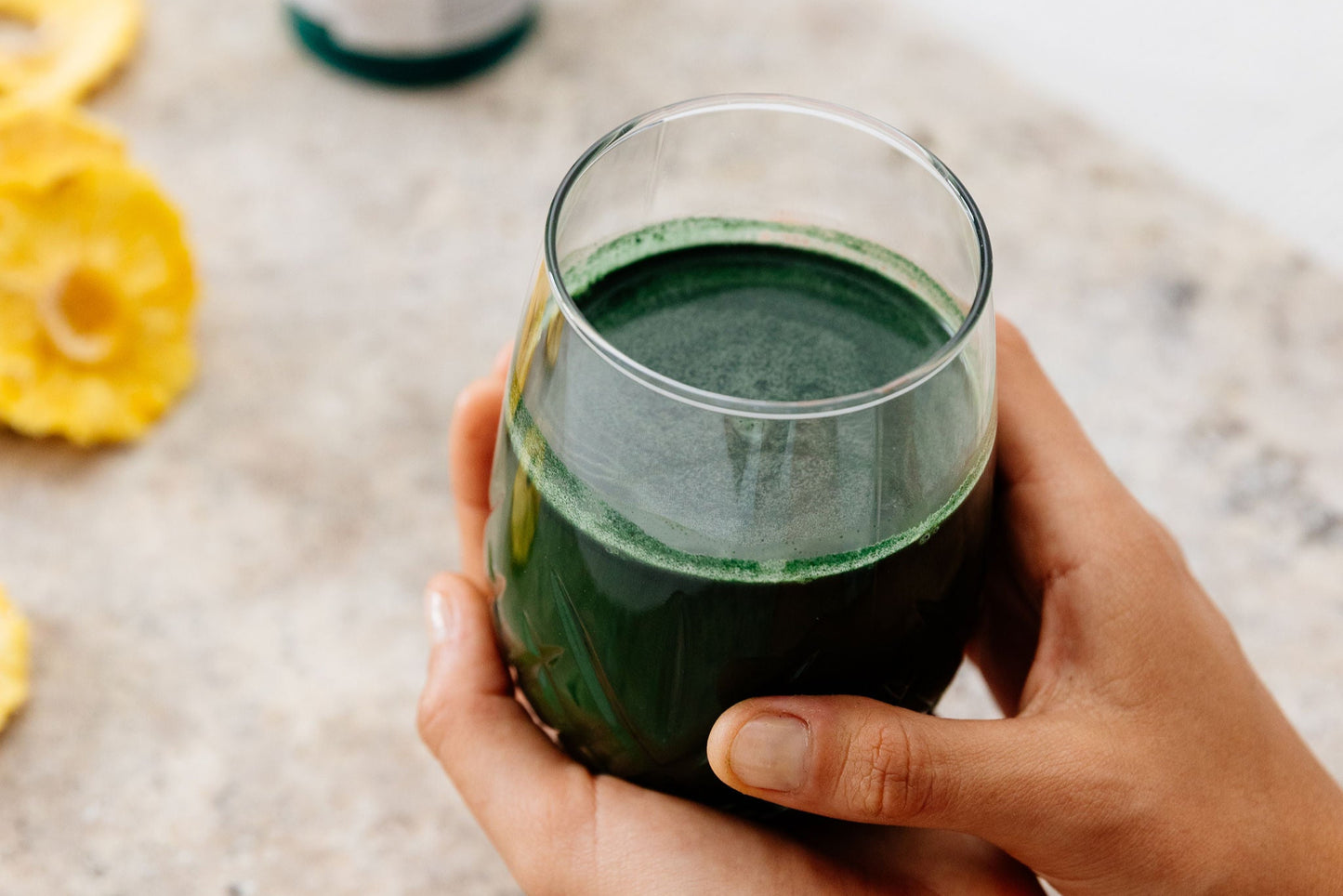 Person holding a glass of Phytality Phytoplankton Super Greens with a bottle and dried fruit on a light surface