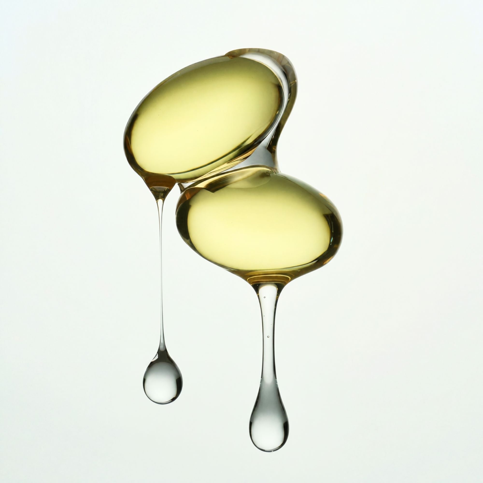 Two droplets of yellow liquid with a third droplet about to join them on a white background
